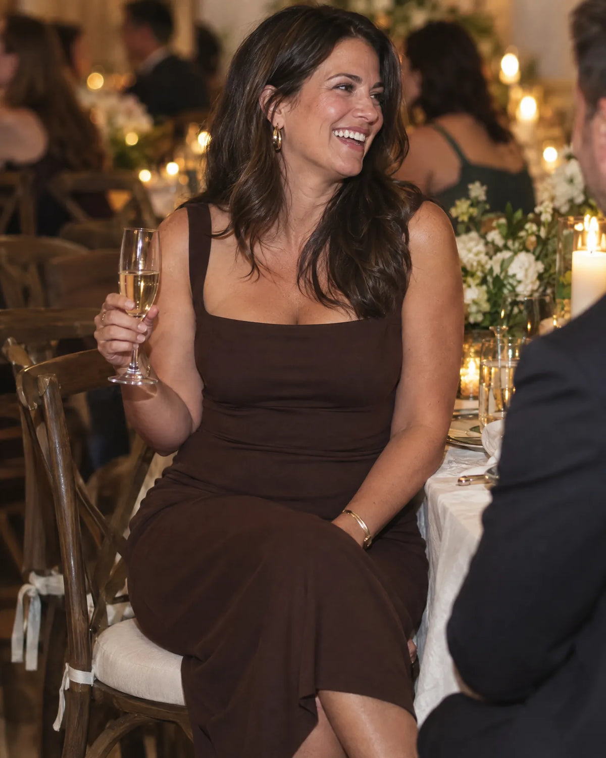 Woman seated at a dinner table in a fitted espresso dress
